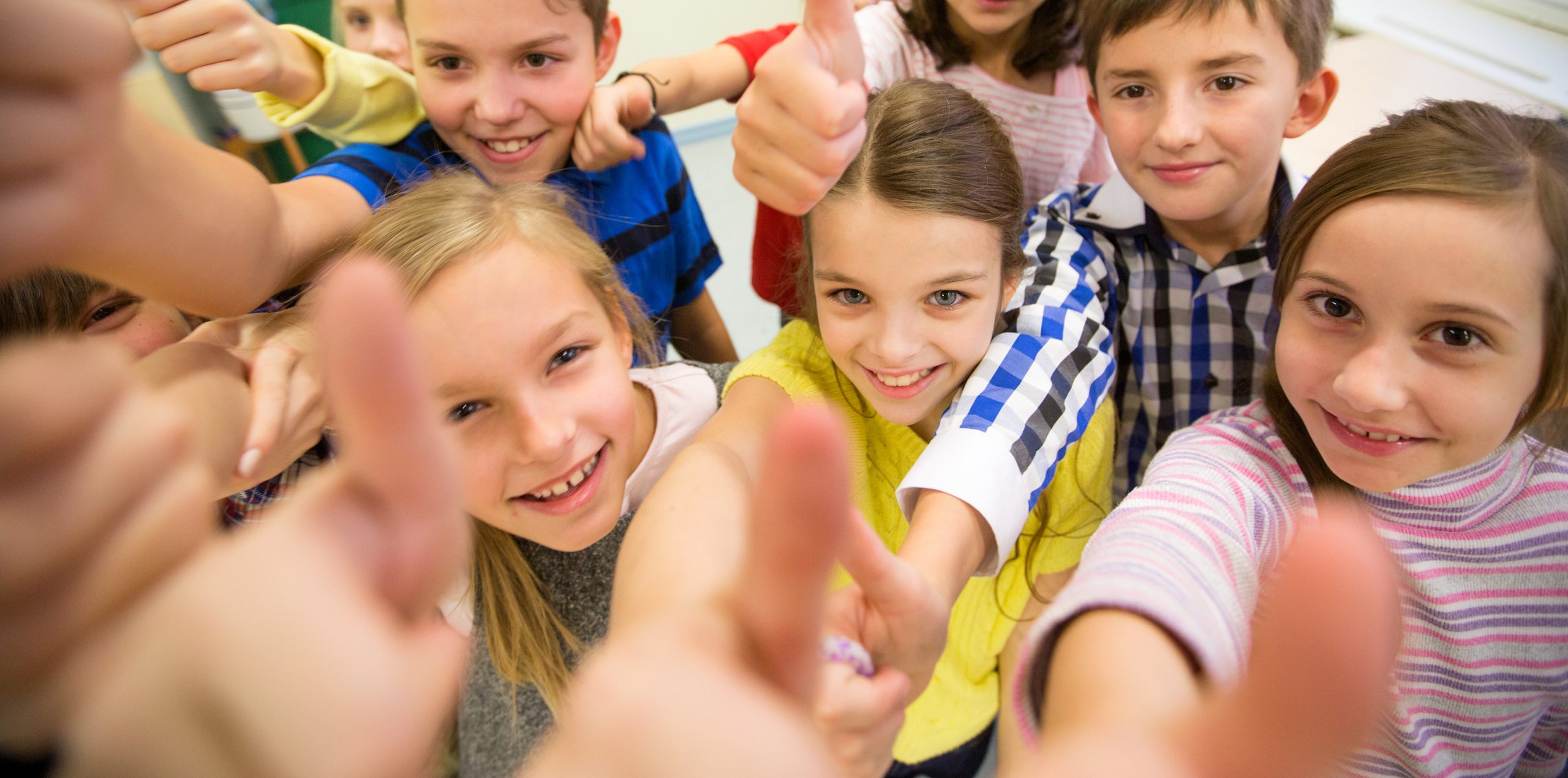 education, elementary school, learning, gesture and people concept - group of school kids and showing thumbs up in classroom